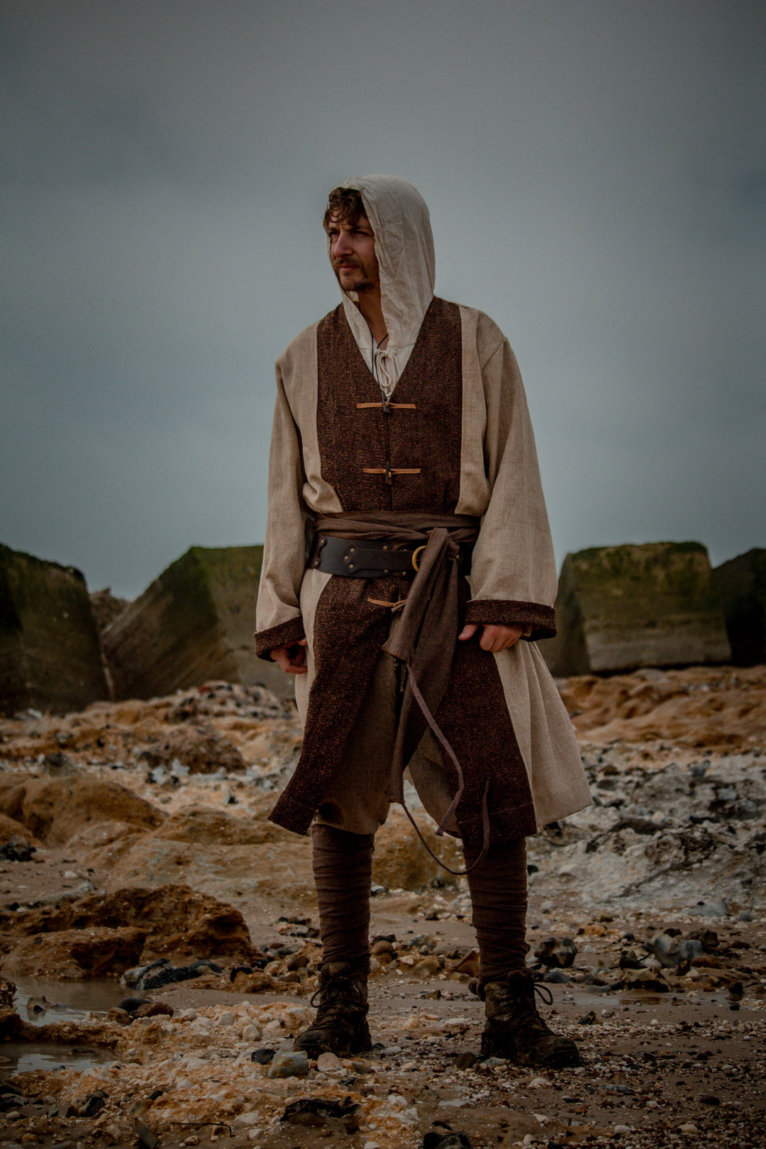 Hooded medieval shirt in natural cotton and linen, worn on rocky terrain.