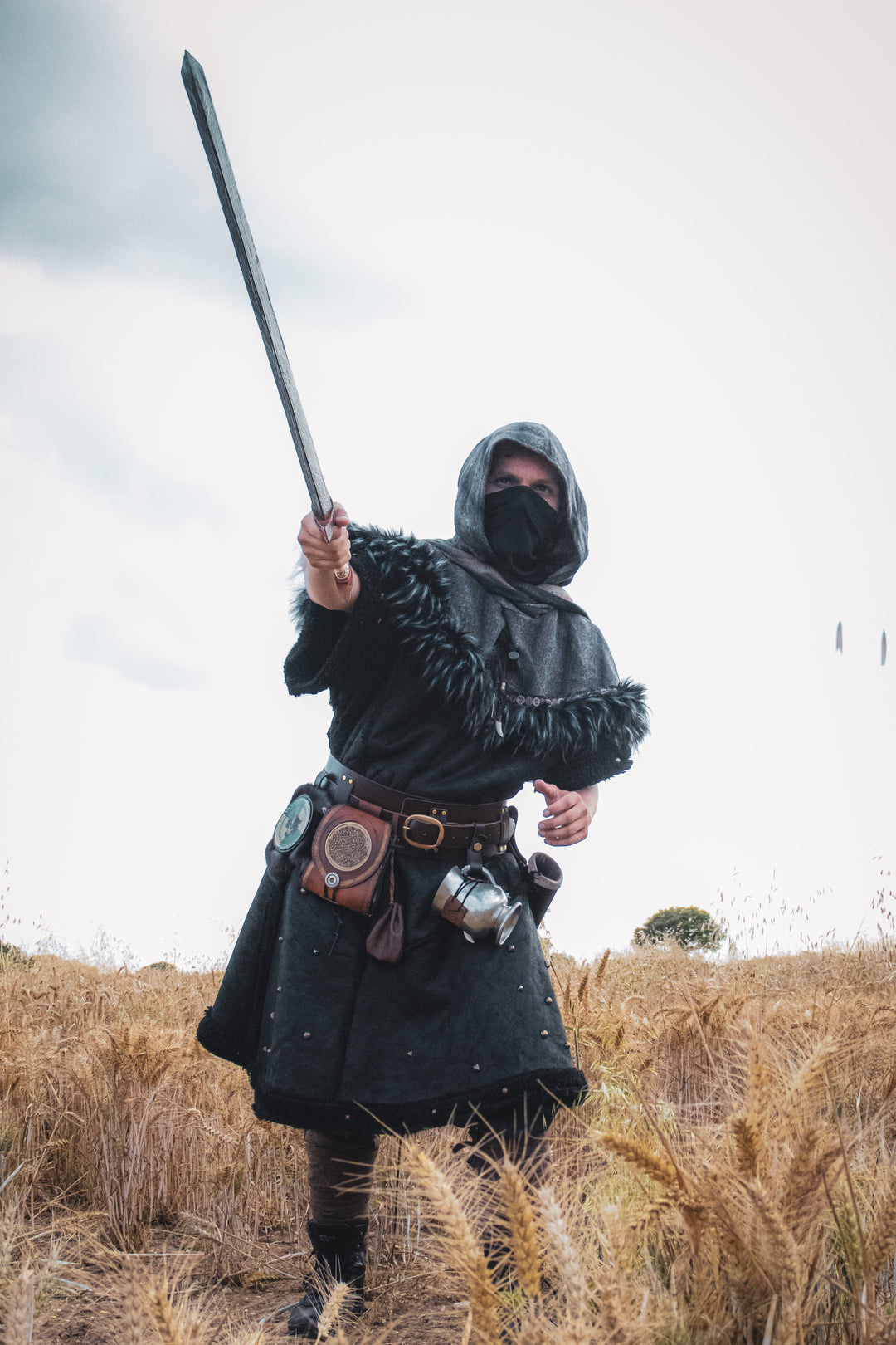 Person in dark medieval attire holding a spear in a field.