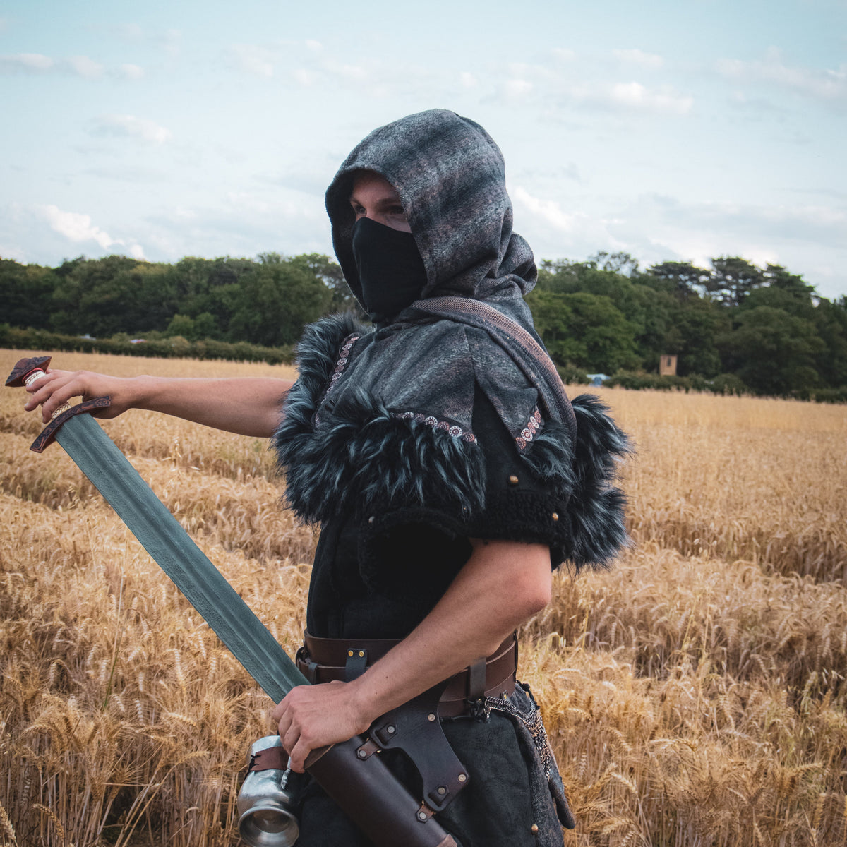 Person in medieval or fantasy costume holding a sword in a field.