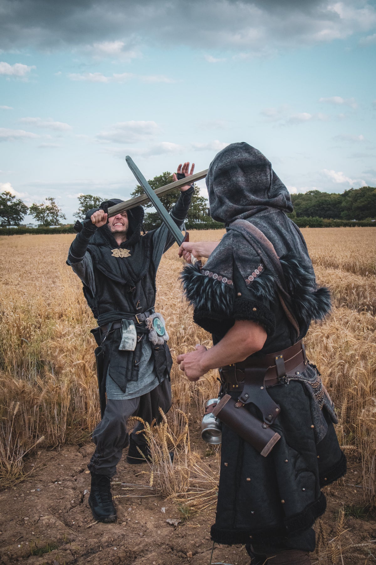 Two people in medieval or fantasy costumes standing in a field with a cloudy sky.