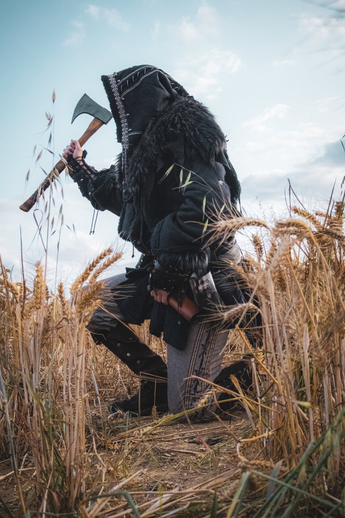 Medieval LARP costume side view featuring a black faux leather jacket, hood and vambraces.