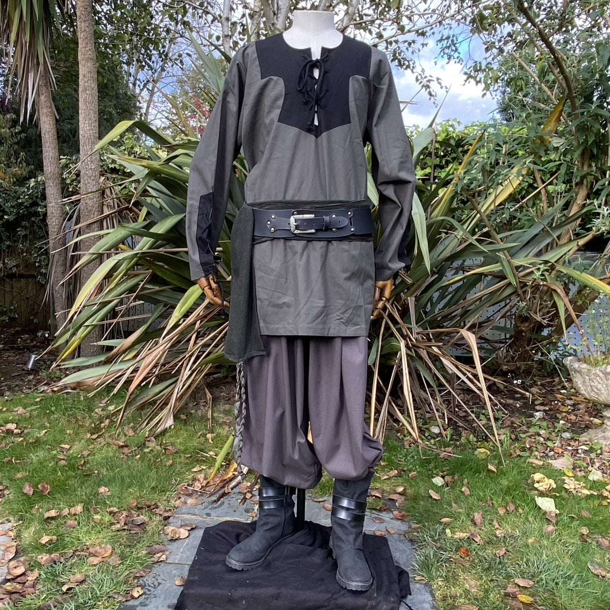 Medieval LARP outfit on mannequin, outdoor garden view, green-black ensemble.