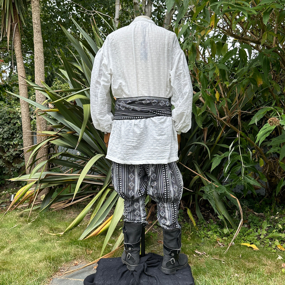 Medieval LARP outfit back view, featuring a white shirt, black and white trousers and matching sash.