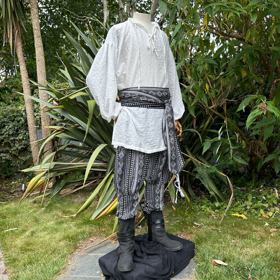 Medieval LARP outfit side view, featuring a white shirt, black and white trousers and matching sash.