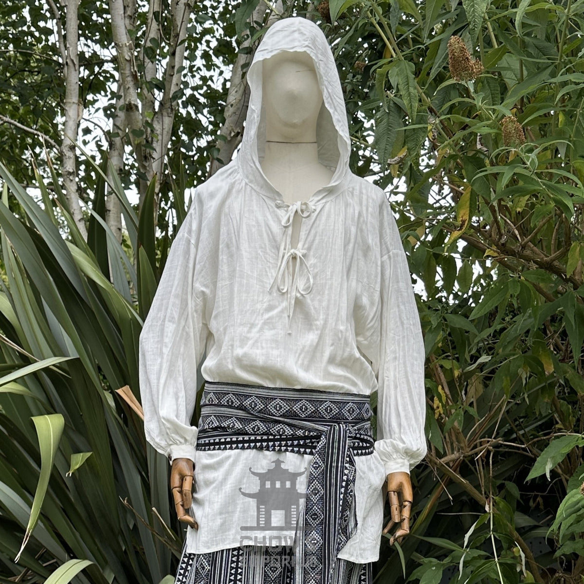 LARP medieval outfit: white hooded shirt, black patterned sash, natural setting.