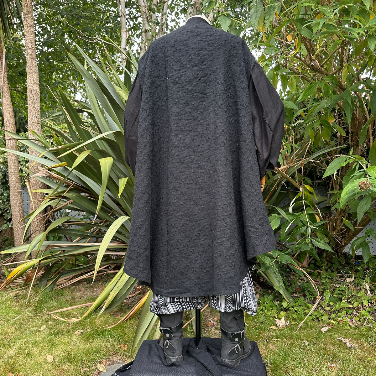 Back view of long black medieval LARP coat with patterned hem and boots.