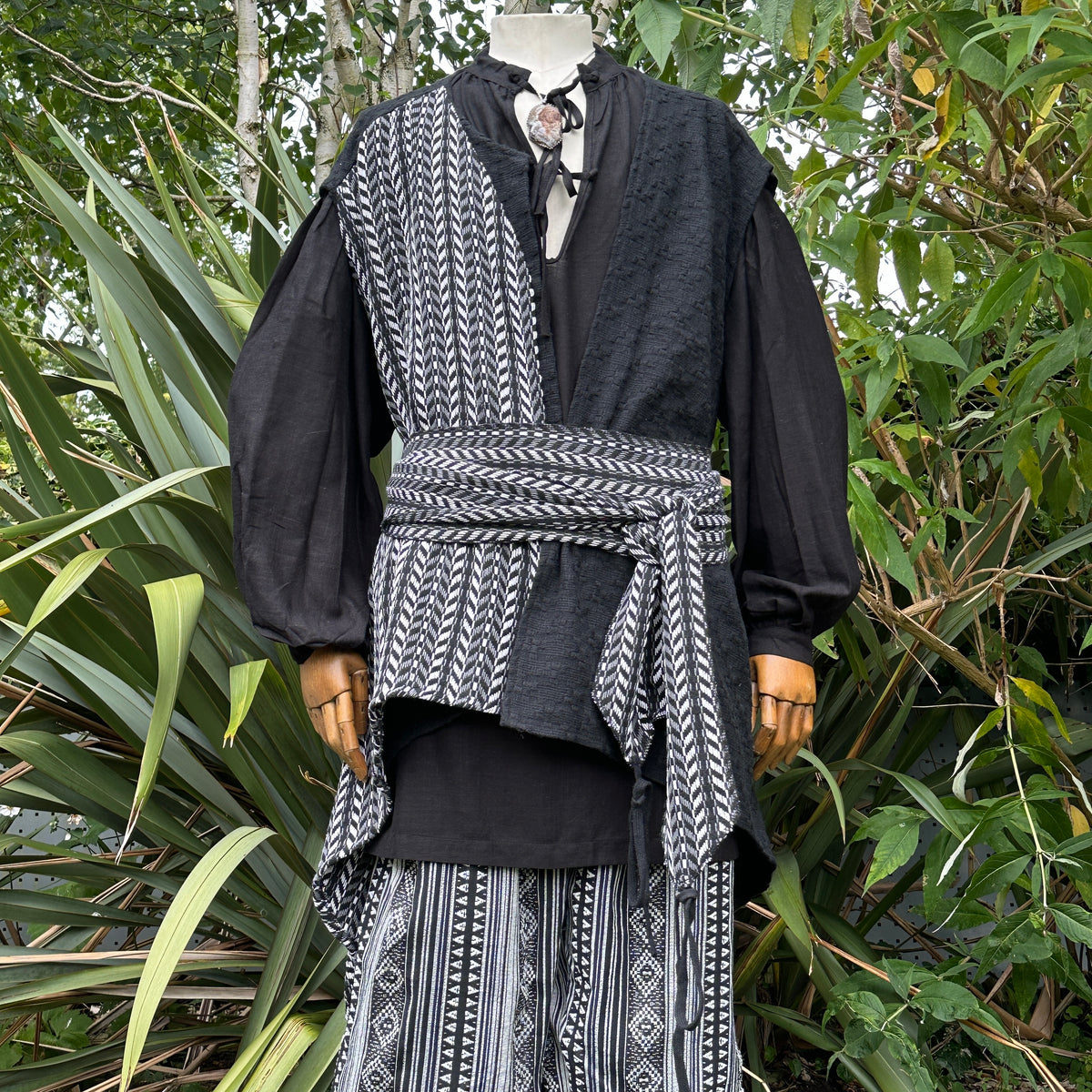 Medieval-style LARP set with patterned sash in a lush garden scene.