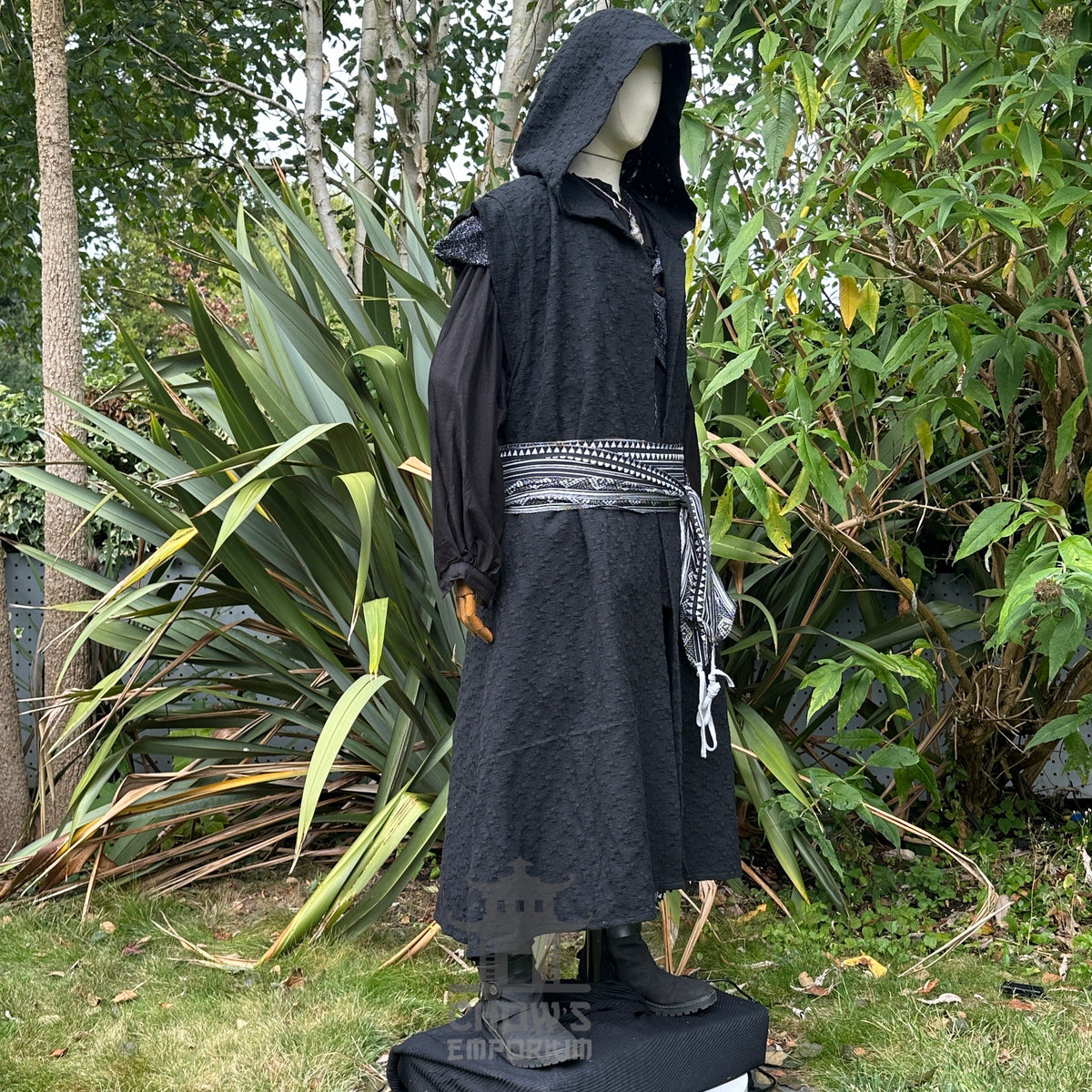 Side view of medieval LARP costume with hooded waistcoat and patterned sash.
