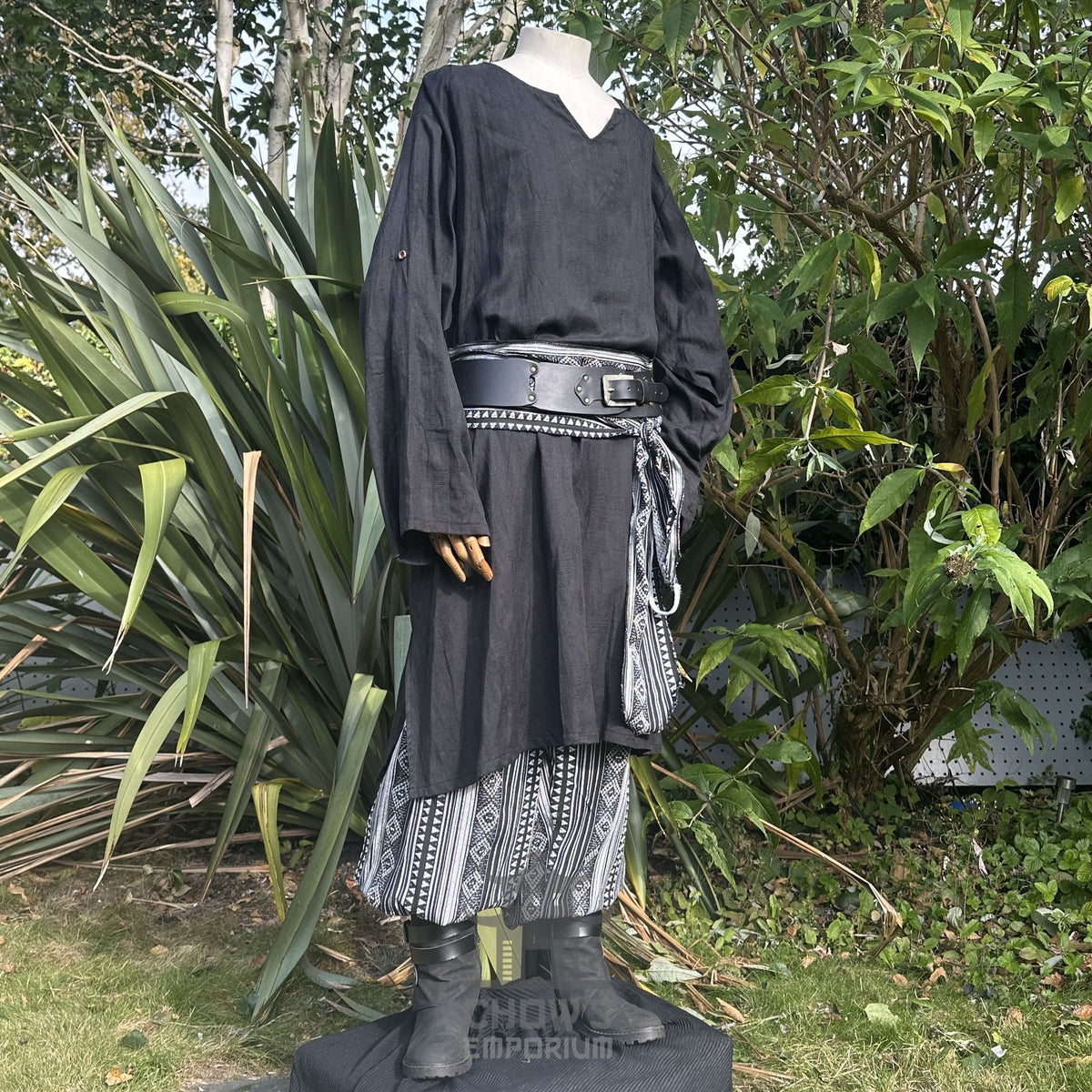 Medieval LARP outfit side view, featuring a black tunic, patterned trousers and sash.
