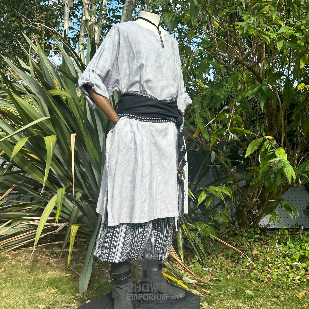 LARP outfit with light grey tunic, patterned trousers, black sash, side view.