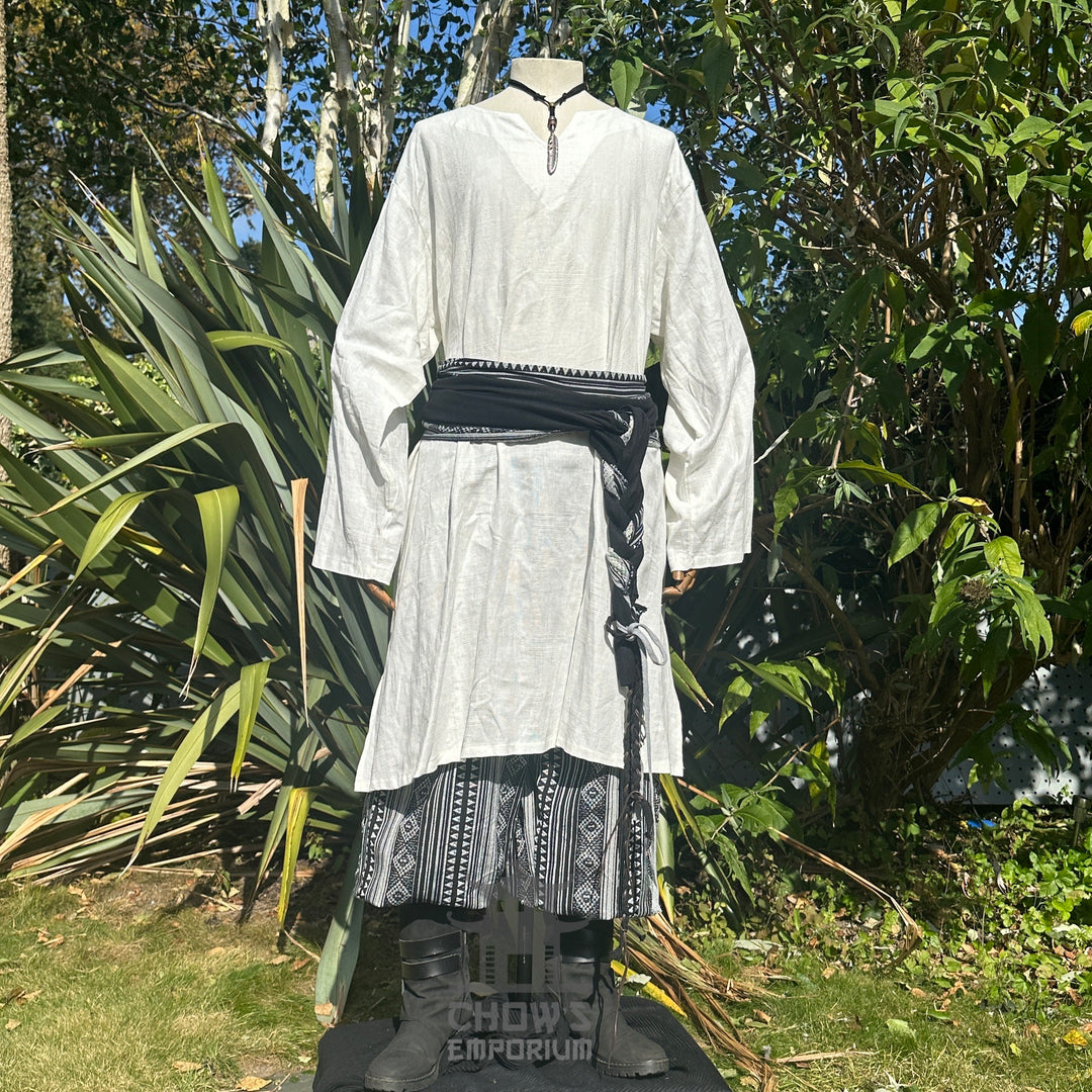 White LARP tunic with black sash and patterned trousers.