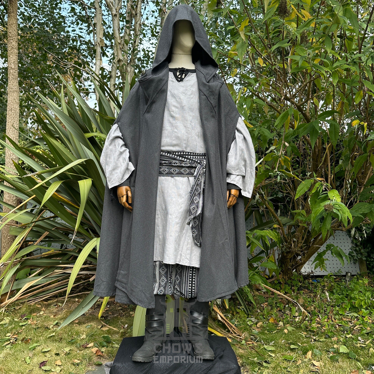 Medieval LARP attire with grey cloak, intricate sash, and lush greenery.