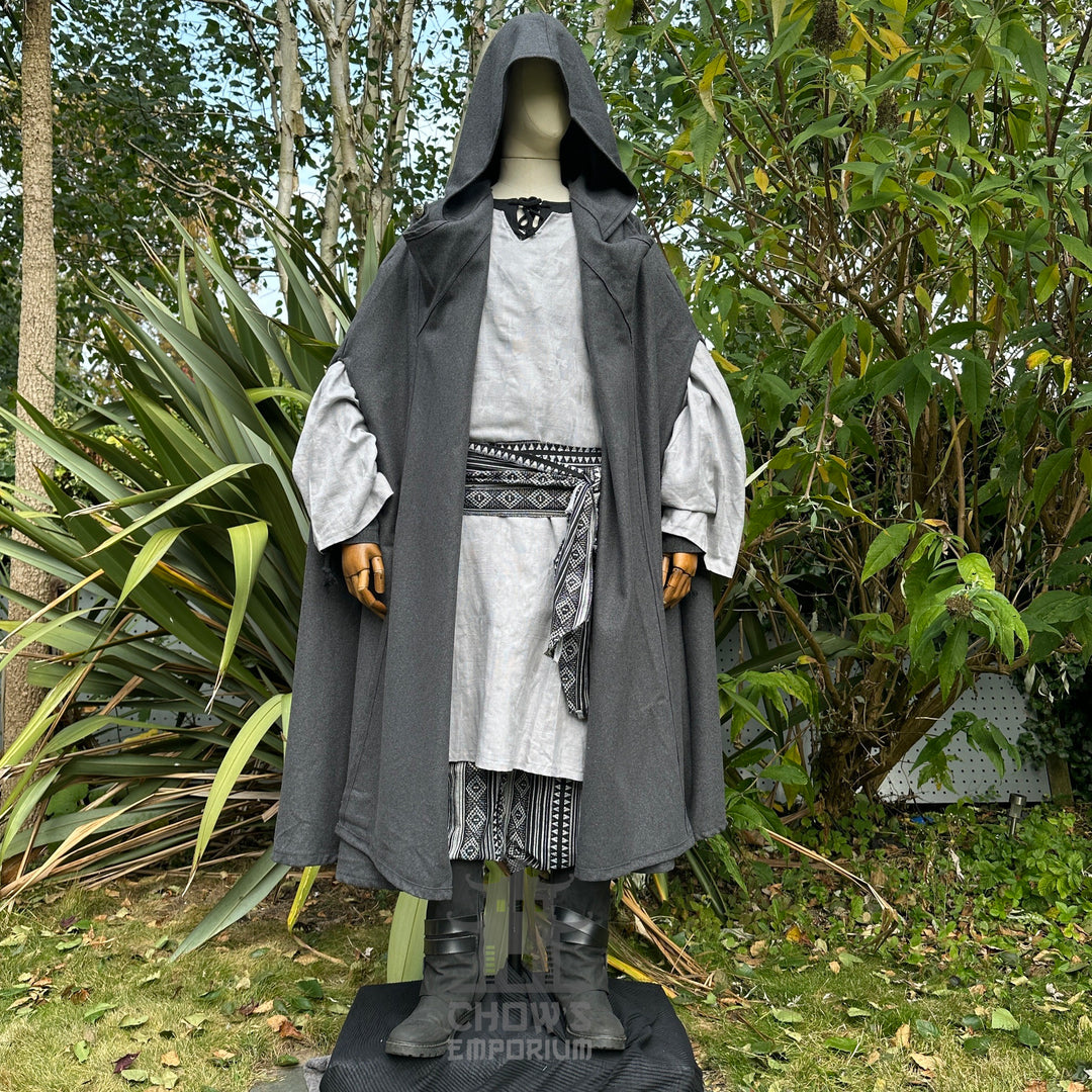 Medieval LARP attire with grey cloak, intricate sash, and lush greenery.