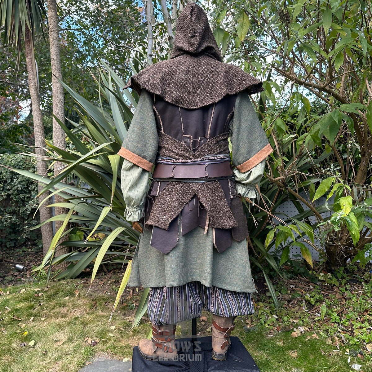 Rear view of green and brown medieval LARP ranger set among trees.