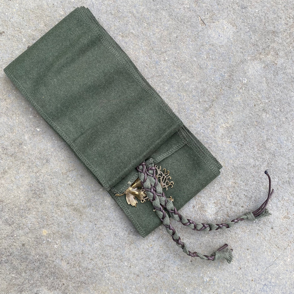Green medieval LARP wrap with woven trim and bronze embellishments on stone surface.
