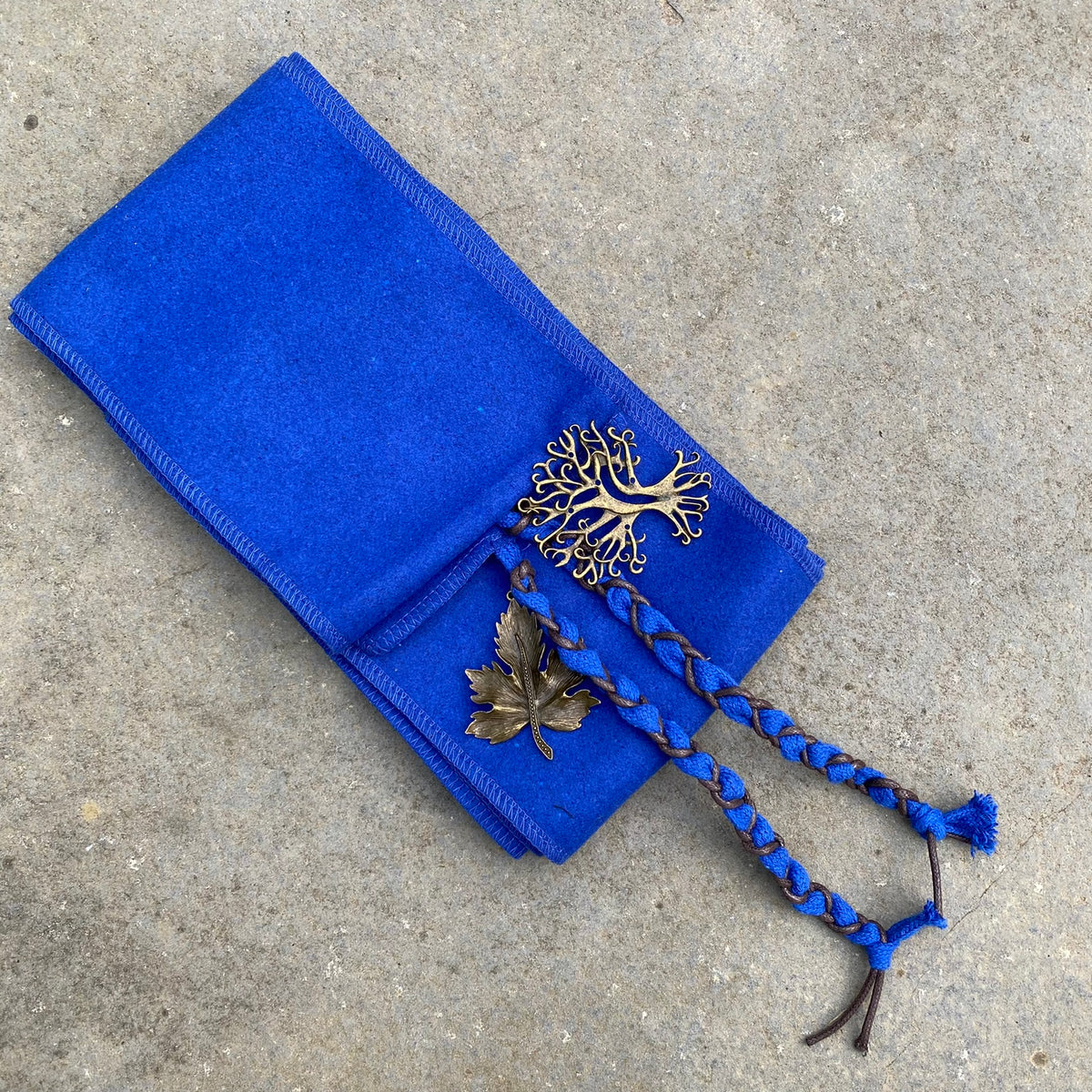 Blue medieval LARP cloak detail with leaf and knotwork accents on stone surface.