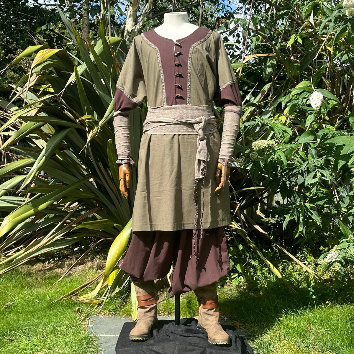 Medieval LARP outfit with tied sash, leafy backdrop, front view.