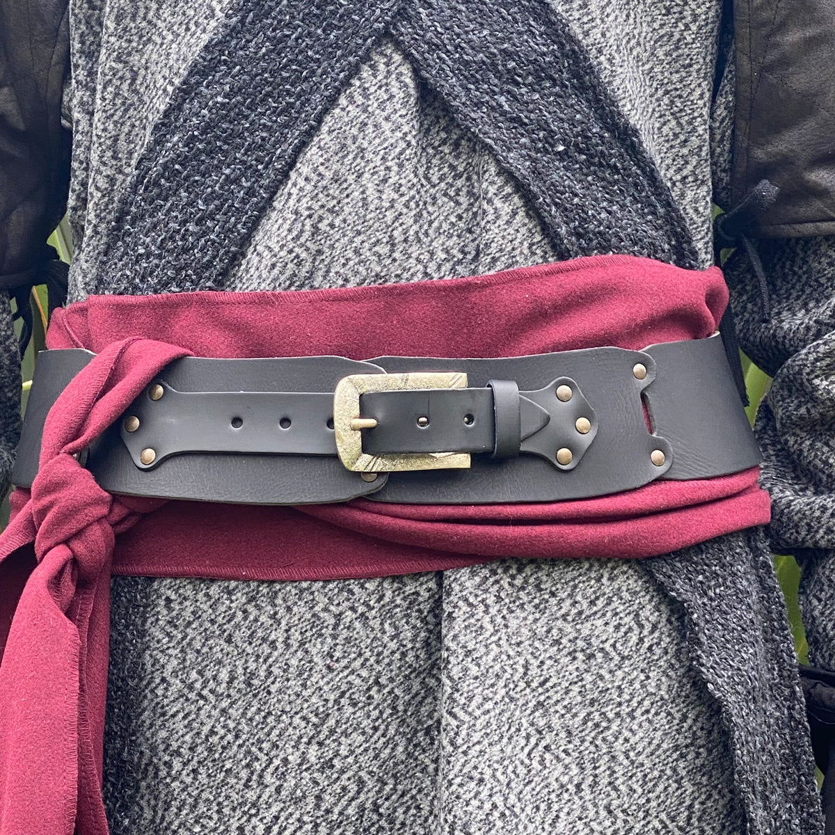 Dark medieval LARP belt and red sash over textured grey jacket close-up.