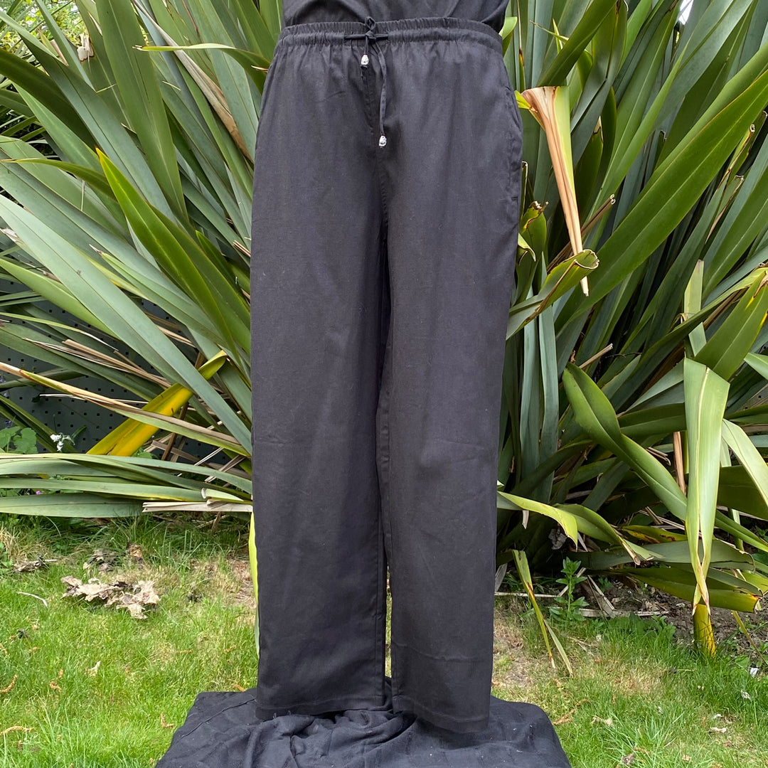 Black medieval LARP pants draped over grass by large green leaves.