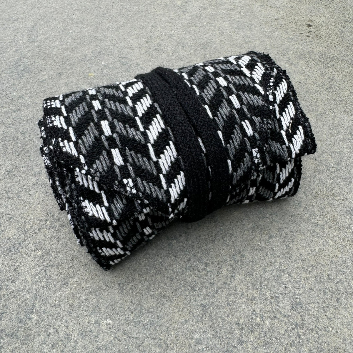 LARP herringbone sash, black and white knitted wool, rolled on stone surface.