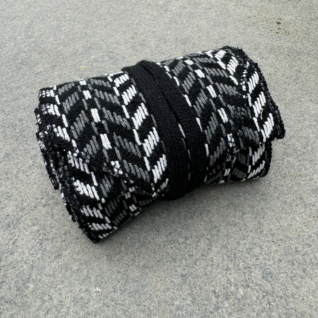 LARP herringbone sash, black and white knitted wool, rolled on stone surface.