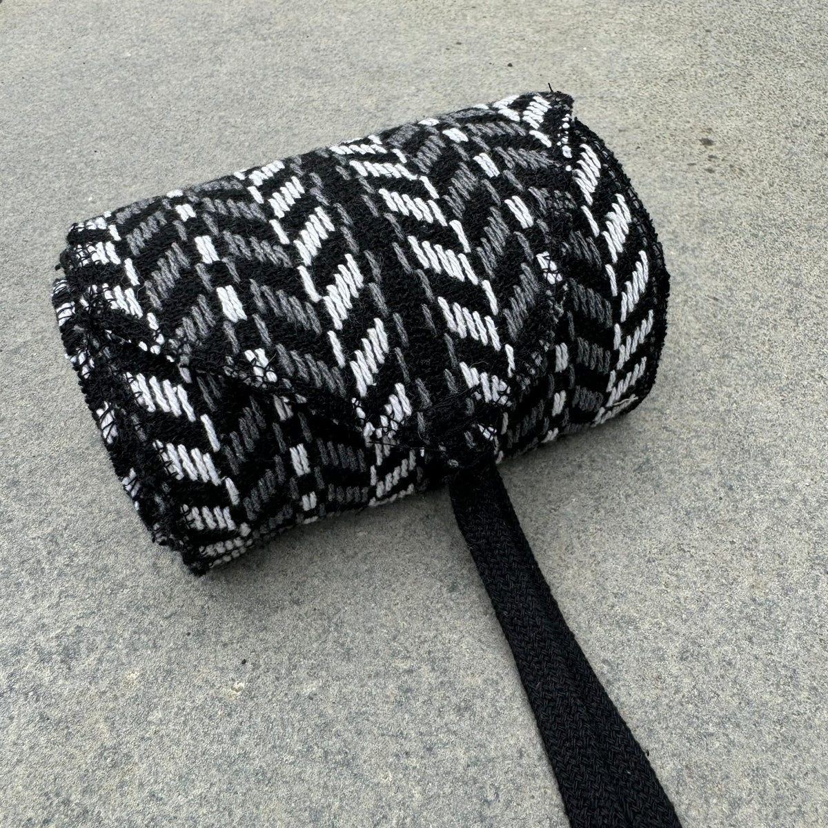 Black and white herringbone LARP sash in knitted wool, rolled up.