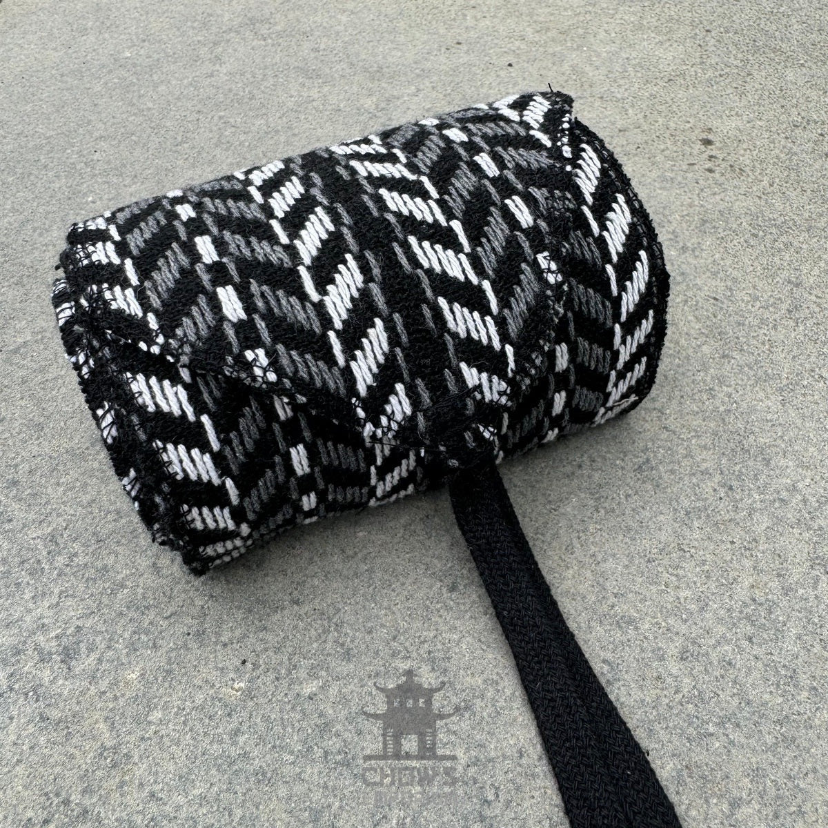 Black and white herringbone sash for LARP rolled up on a stone surface.