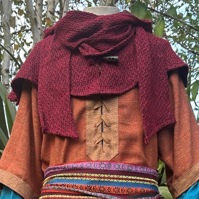 Medieval LARP costume with red knit hood, orange tunic, and colorful sash.