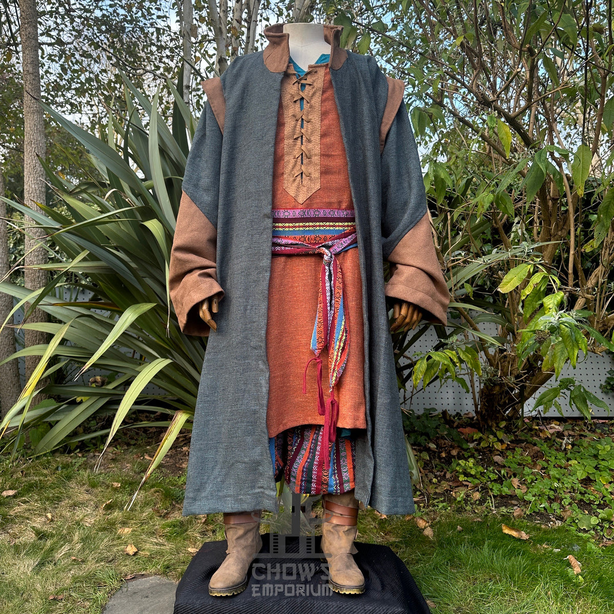 Outdoor LARP set view; multicolored sash over brown and blue medieval robe.