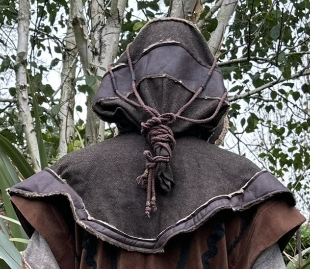 Back view of medieval LARP hood with rope detail against a forest backdrop.