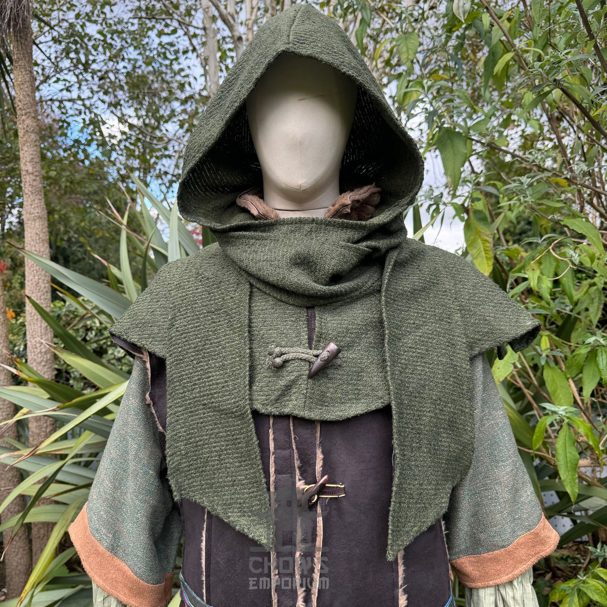 Medieval LARP ranger hooded tunic close-up with green foliage backdrop.