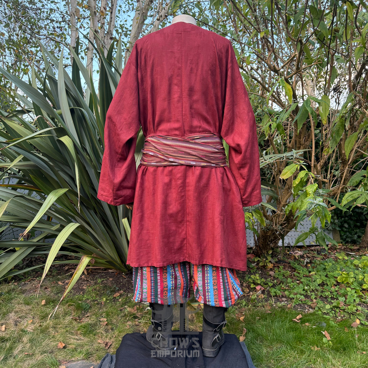 Medieval LARP outfit back view, featuring a red tunic, multi-striped trousers and sash.