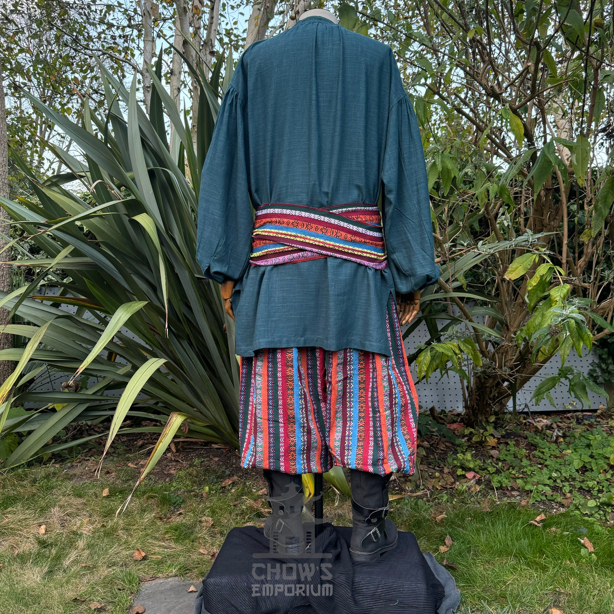 Medieval LARP outfit back view, featuring a teal shirt, multi-striped trousers and matching sash.