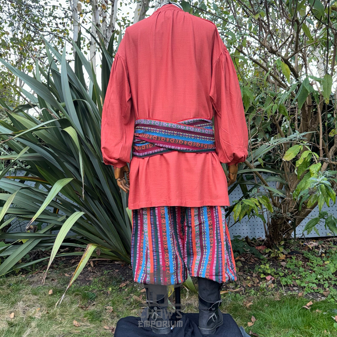Medieval LARP outfit back view, featuring an orange shirt, multi-striped trousers and matching sash.