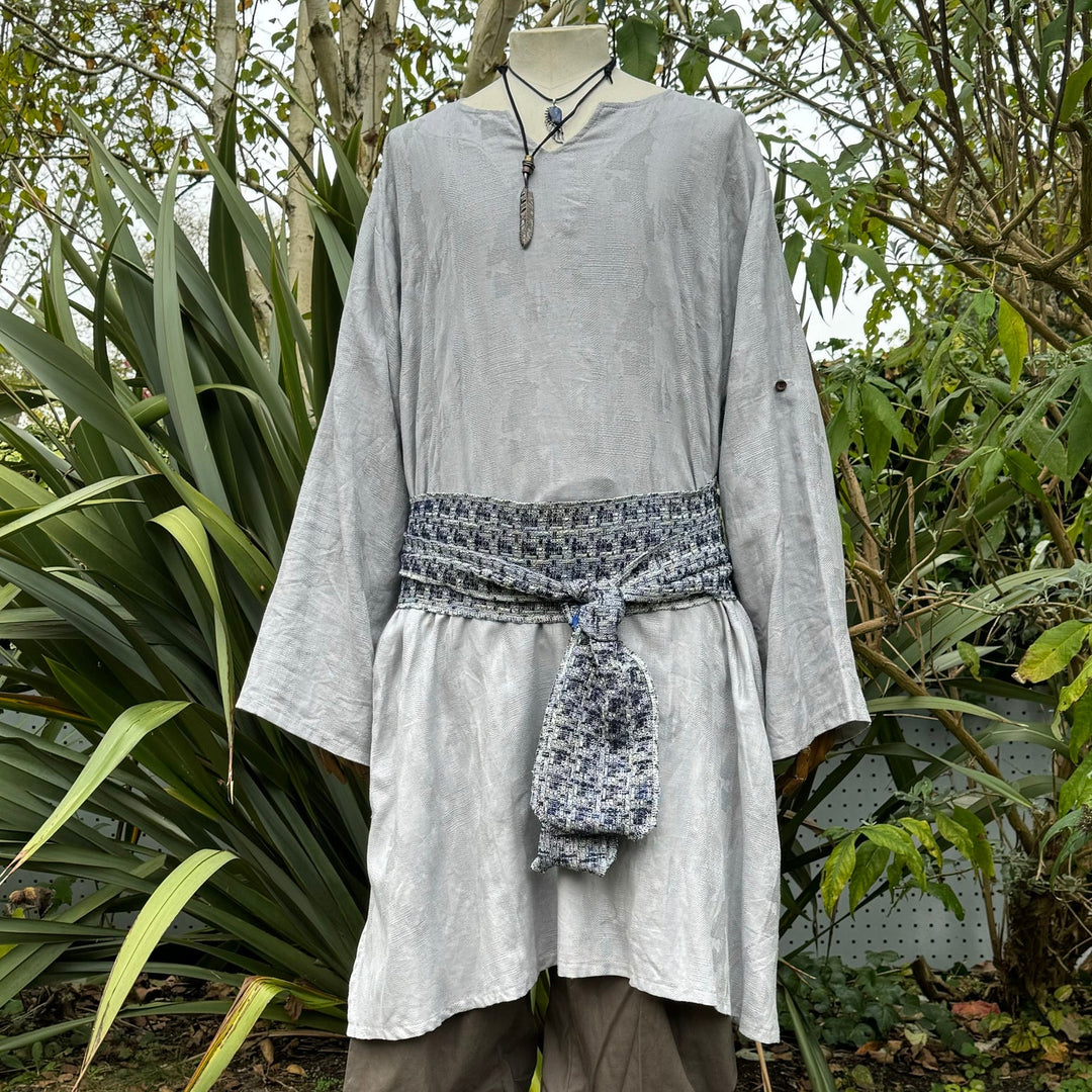 Front view of grey LARP tunic with patterned sash among garden greenery.