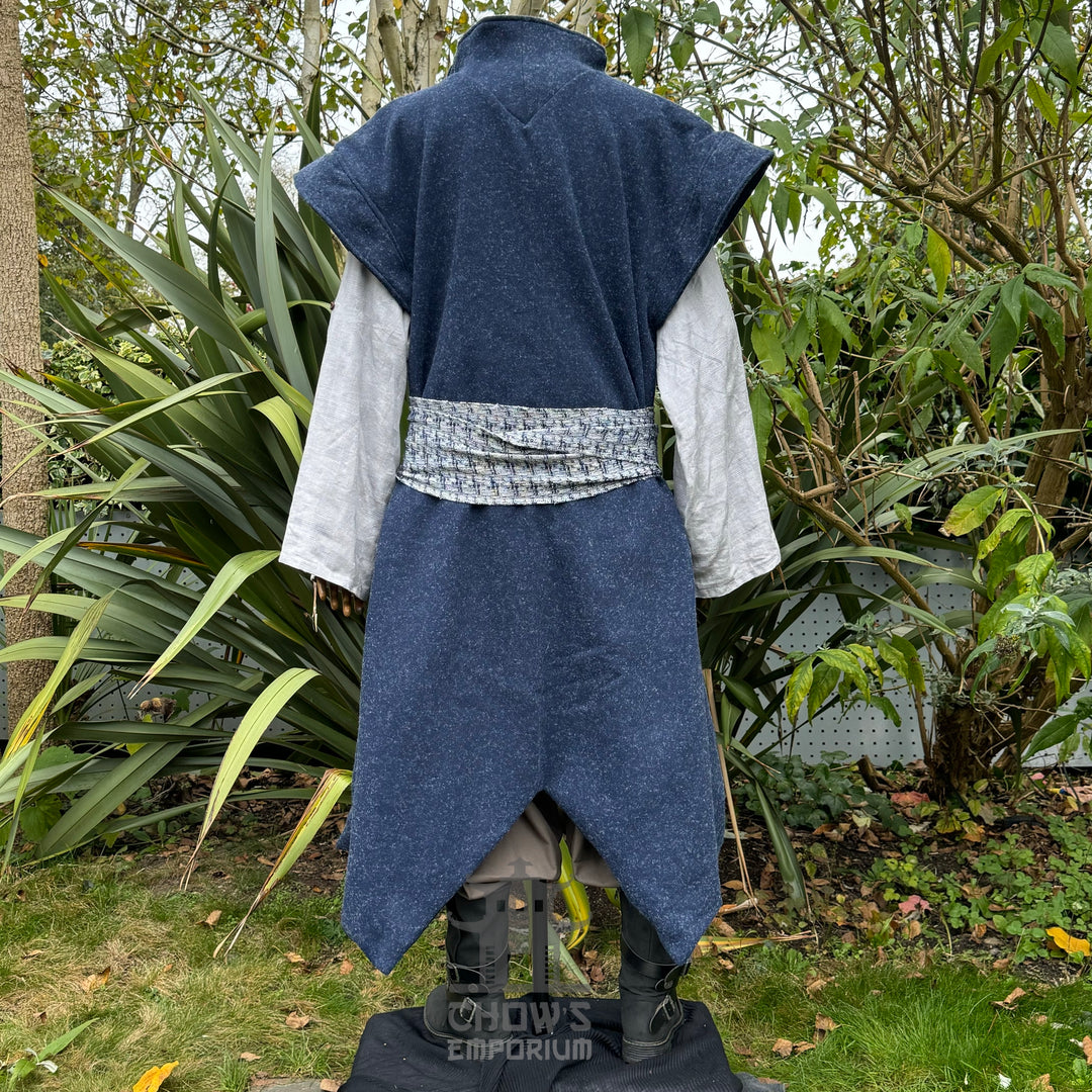 Medieval LARP costume back view, featuring a blue waistcoat, tunic, trousers, arm wraps, sash.