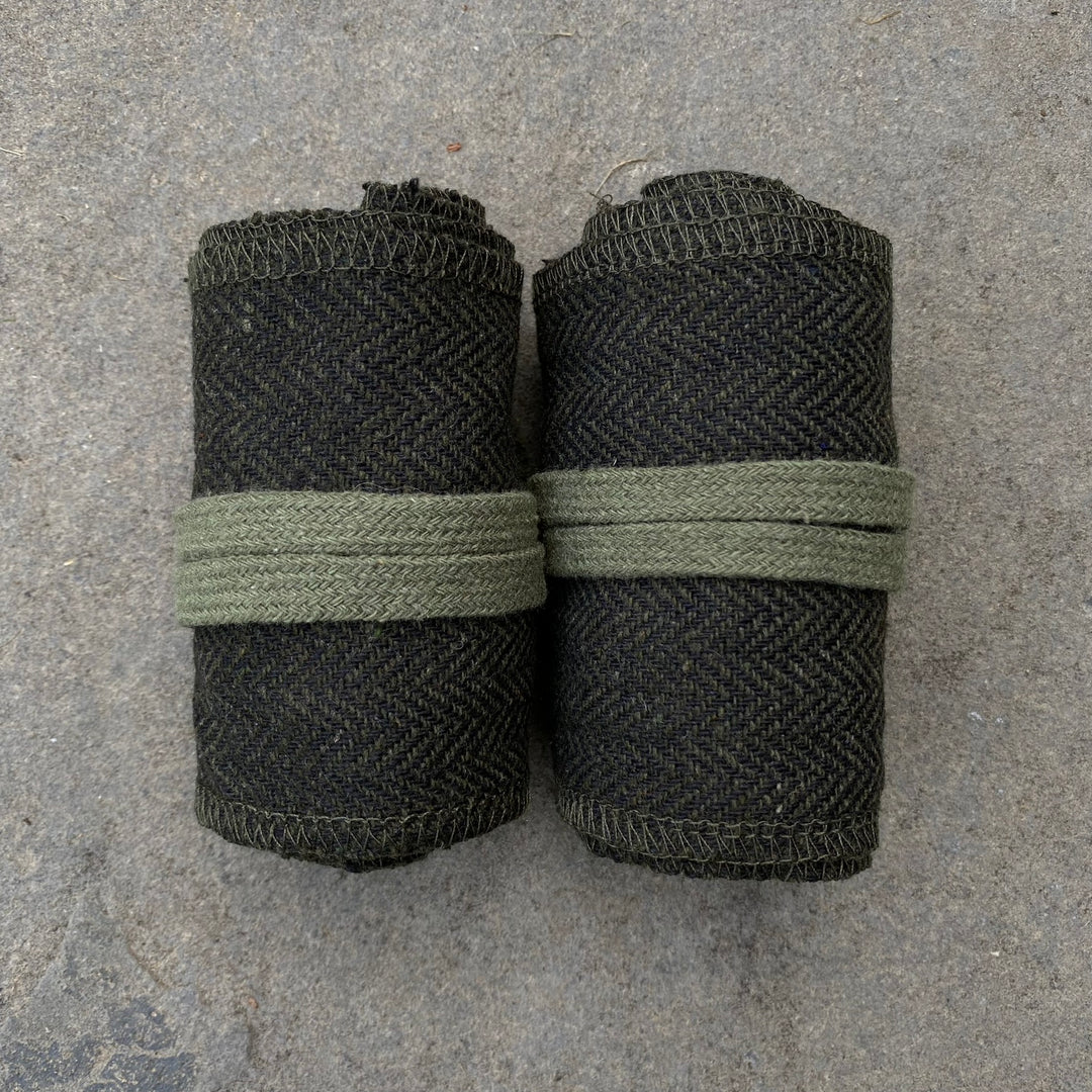 Rolled medieval LARP wraps in green herringbone pattern on stone surface.