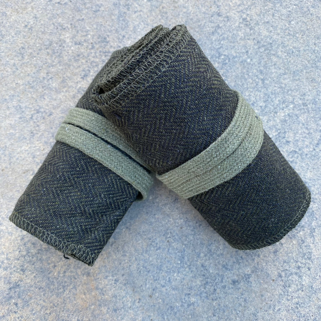 Rolled medieval LARP wraps, green-black herringbone on a stone surface.