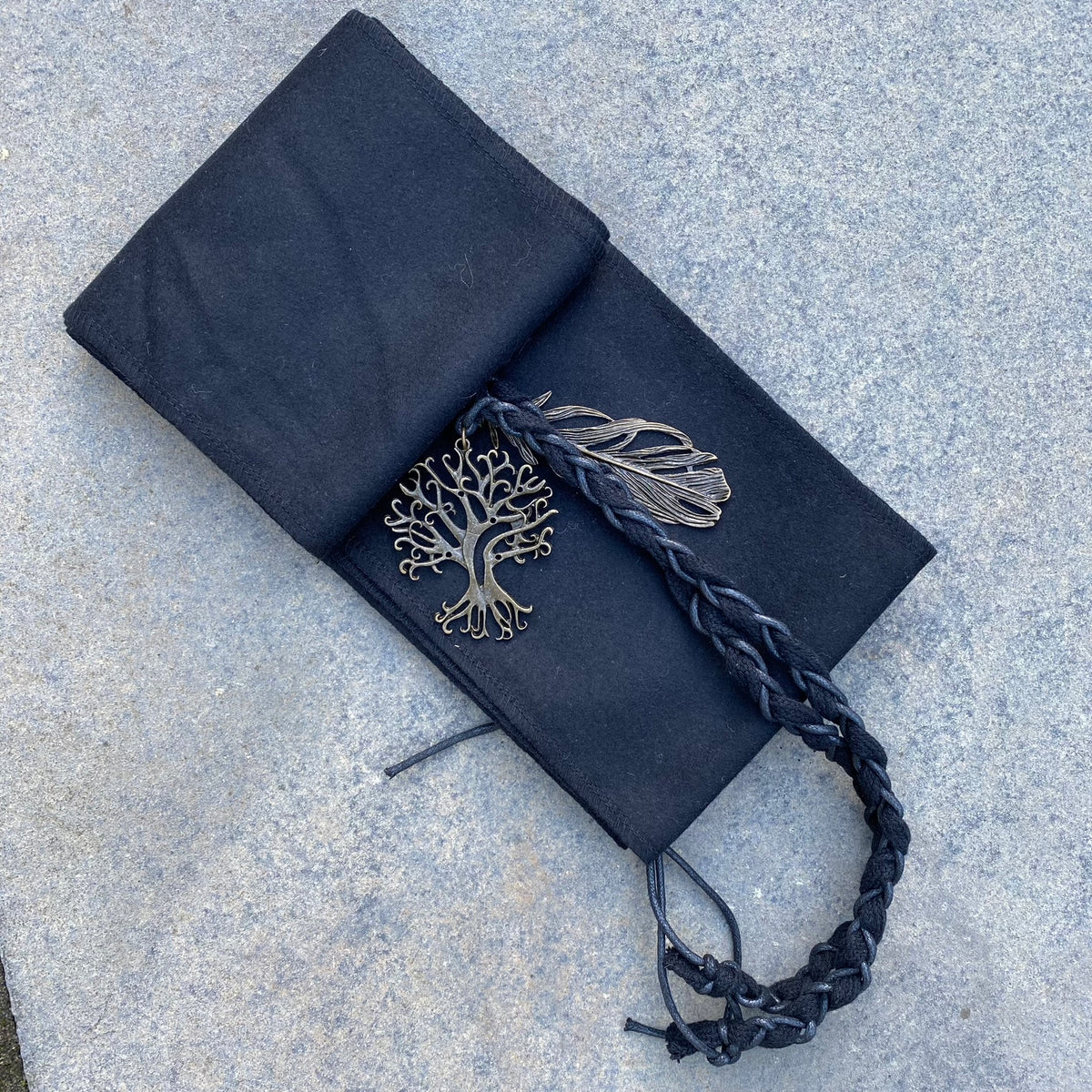 Braided medieval LARP sash with metal tree and feather details on stone background.