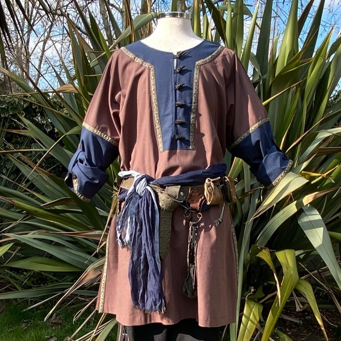 Front view of medieval LARP tunic with blue trim and rustic accessories.
