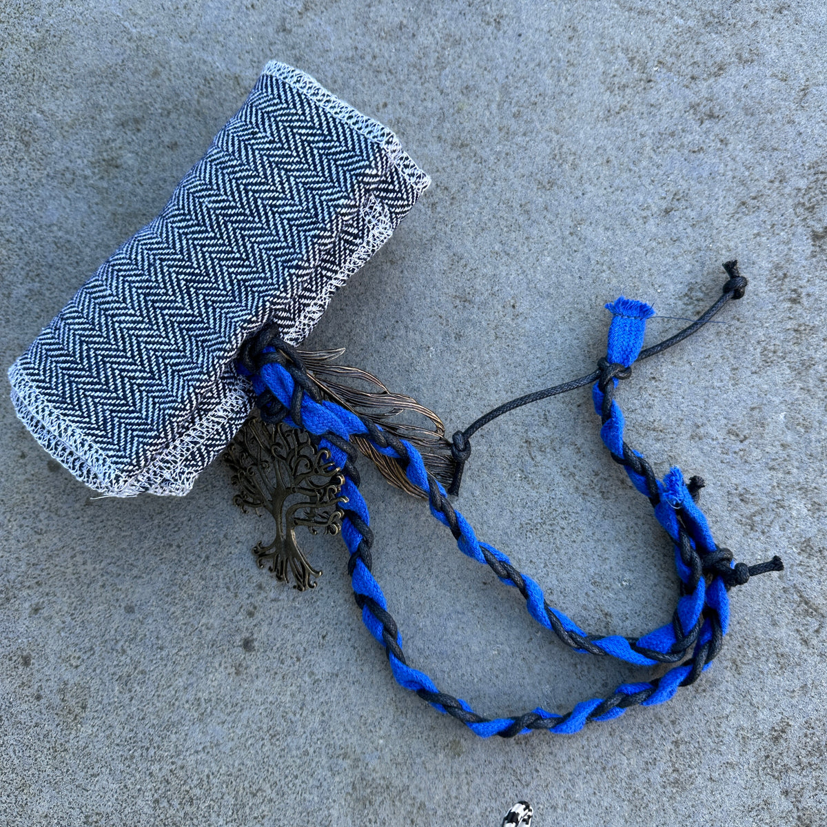 Blue wool LARP sash with tree charm and braided details on grey backdrop.
