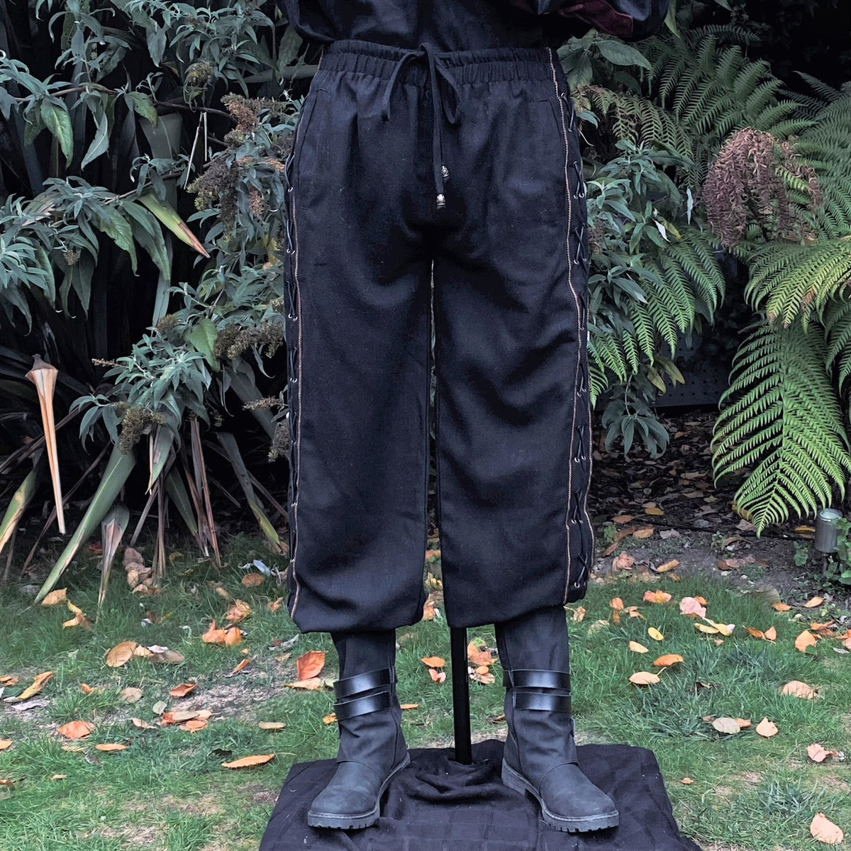 Black LARP pants with side lace detail, front view amidst garden foliage.