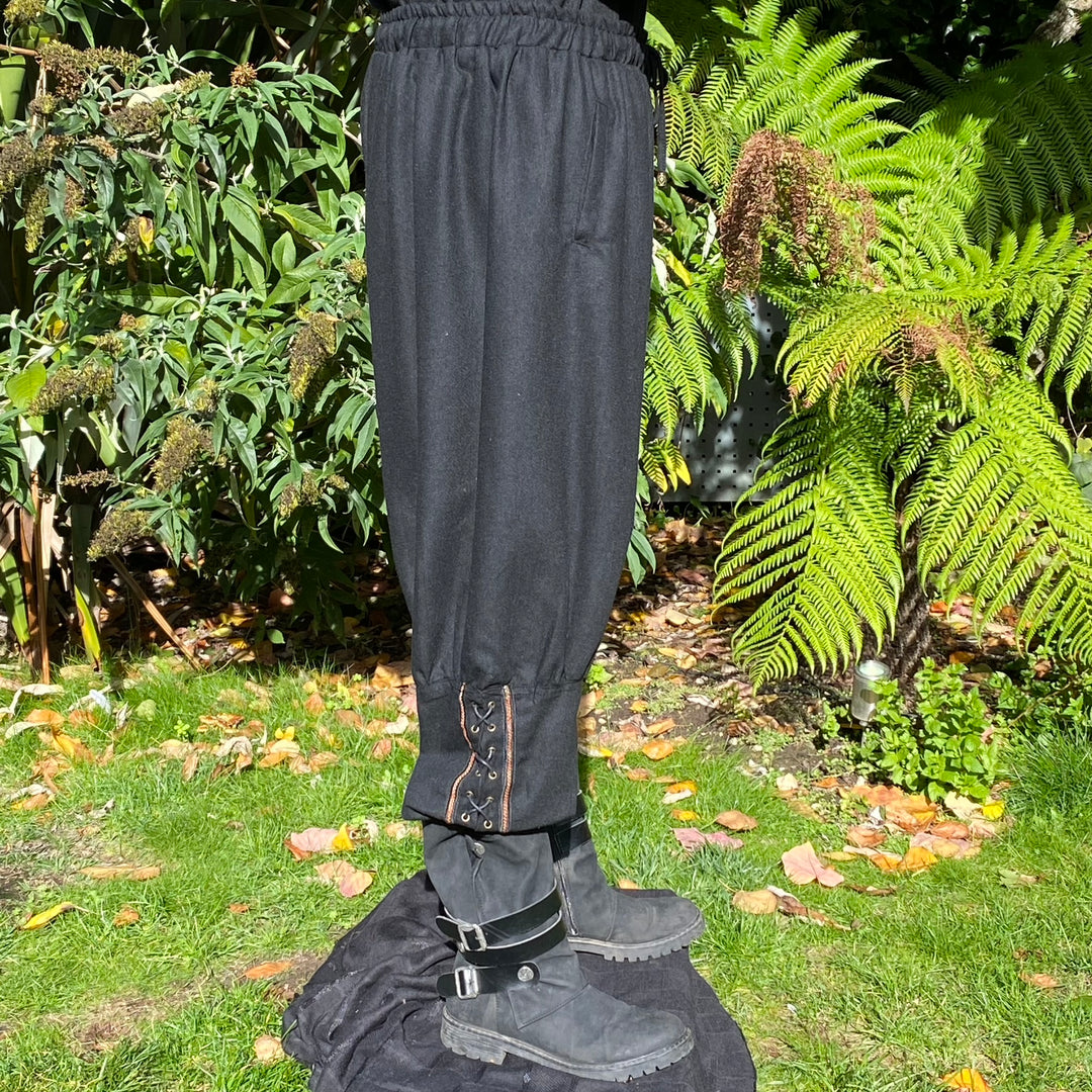Black LARP pants with lace-up cuffs on grass, side view.