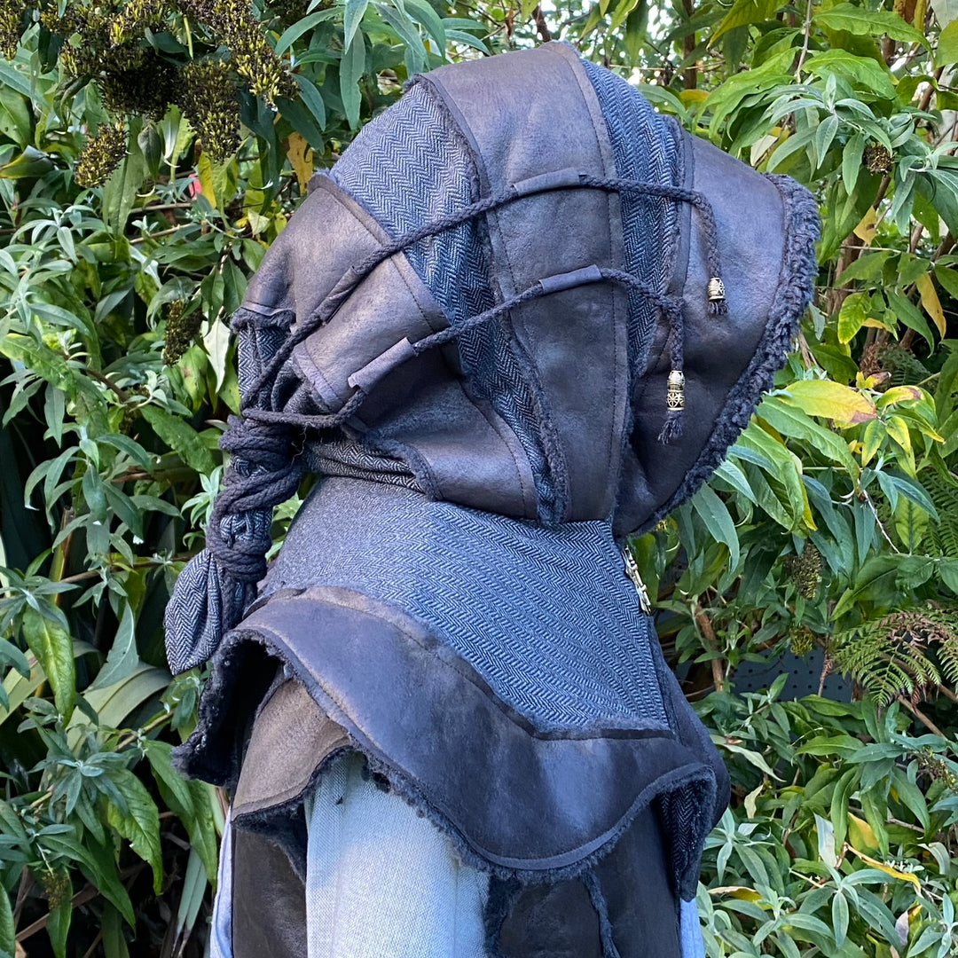 Dark LARP hood with textured fabric and beads, side view against greenery.