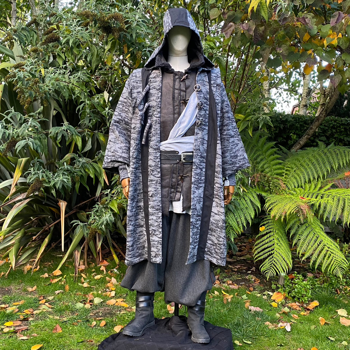Medieval LARP costume with layered robe, hood; garden setting backdrop.