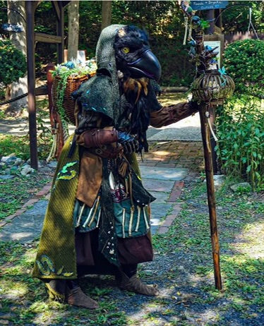 Druid LARP costume with green hood, vambraces, and rustic accessories, side view.