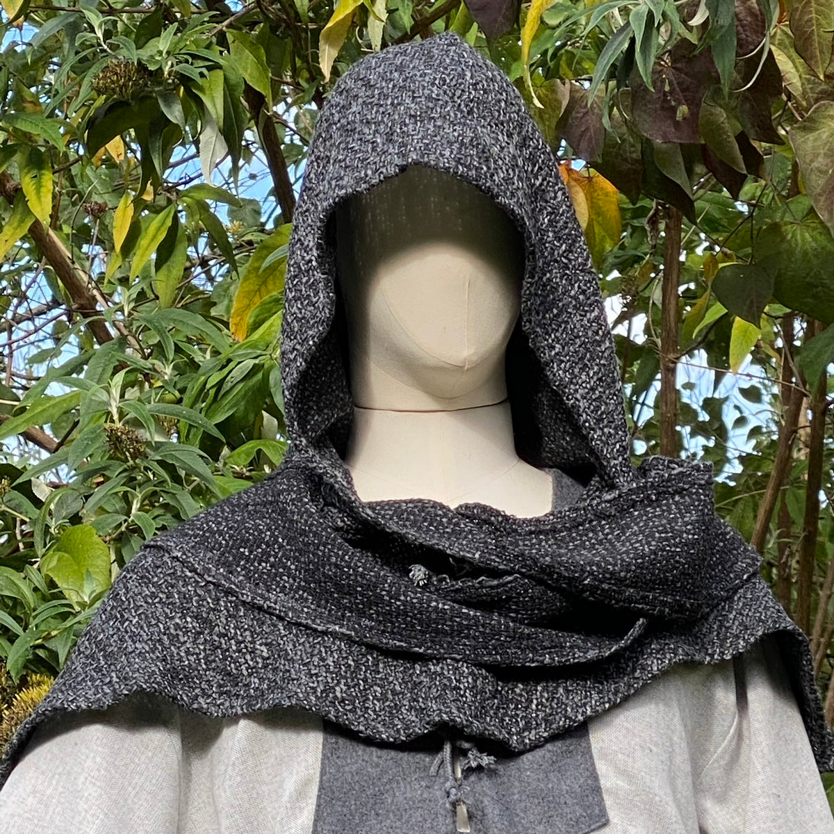 Medieval LARP hooded mantle on mannequin surrounded by greenery.