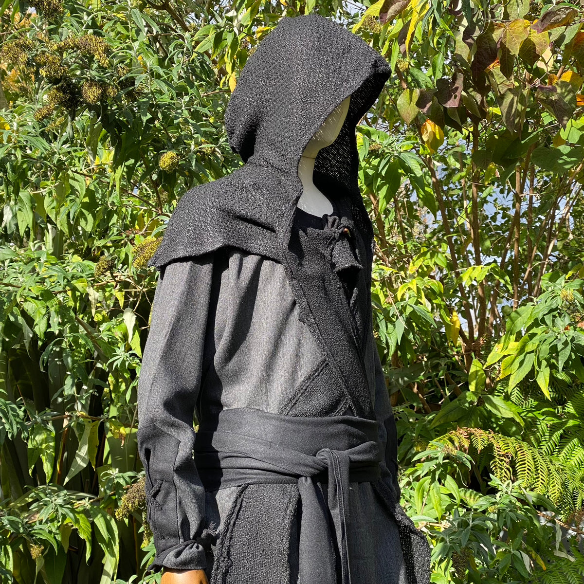 Medieval LARP outfit with hooded mannequin, side view among greenery.