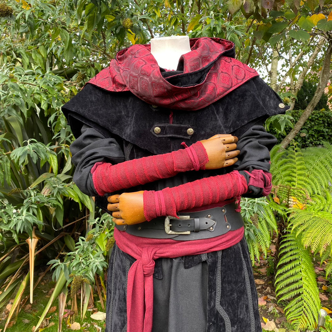 Medieval red arm wraps on mannequin with black cloak, LARP attire detail.