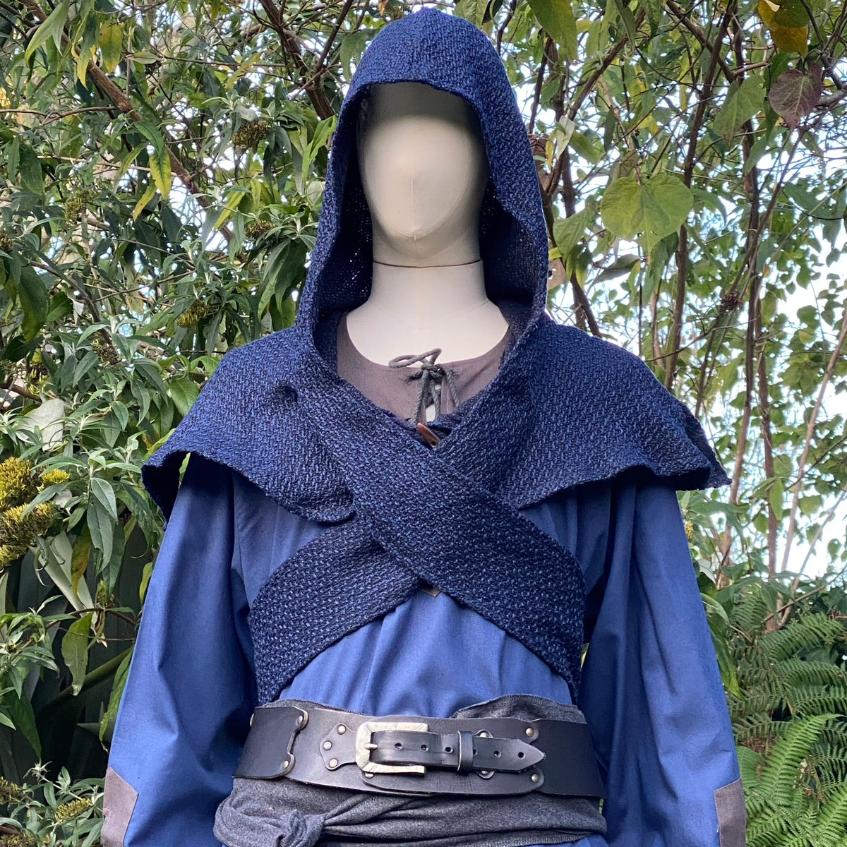Medieval LARP outfit with blue hood and waistcoat, leafy background.